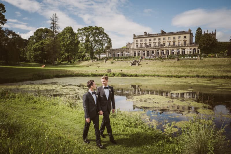 Same-sex couple embracing with Italian wedding venue in the background